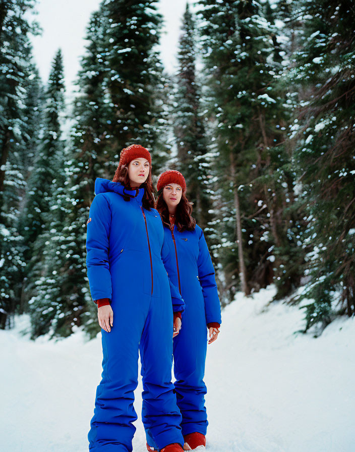 Pair in Blue Winter Outfits with Red Beanies in Snowy Pine Forest