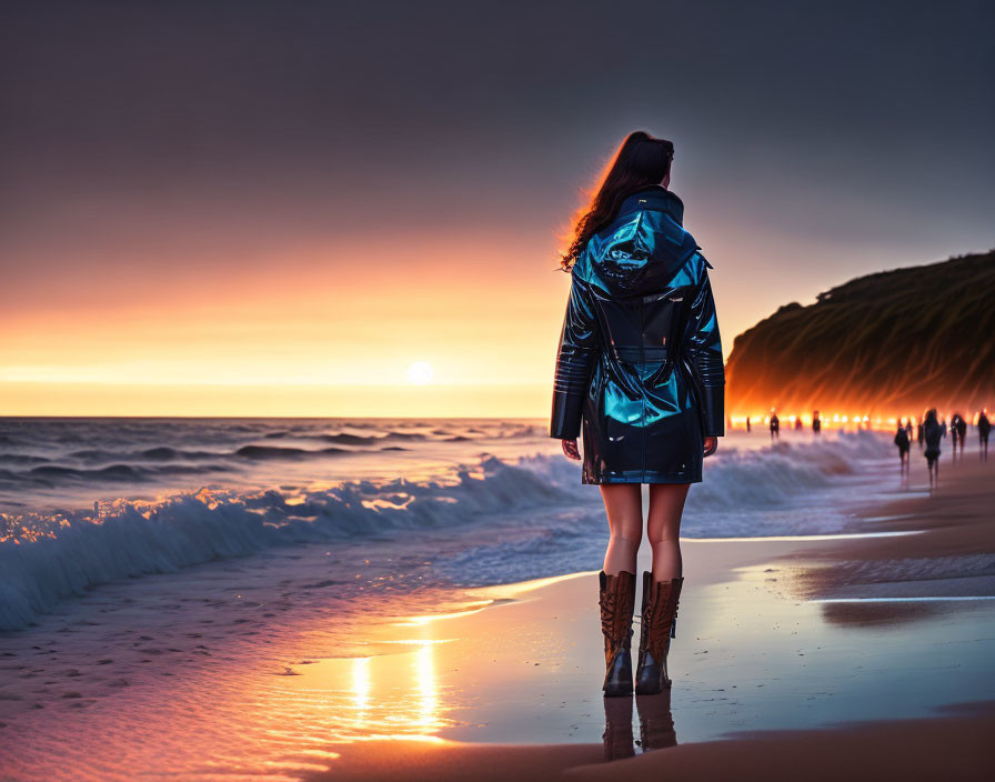 Person in Blue Jacket Waves on Beach at Sunset with Others Walking