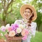 Glamorous woman with bold makeup and blonde hair surrounded by colorful flowers and jewelry on vibrant green floral