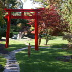 Tranquil garden with red archway, lush greenery, colorful flowers, and meandering stream