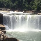 Tranquil waterfall scene with sunlight, trees, and rocky pool