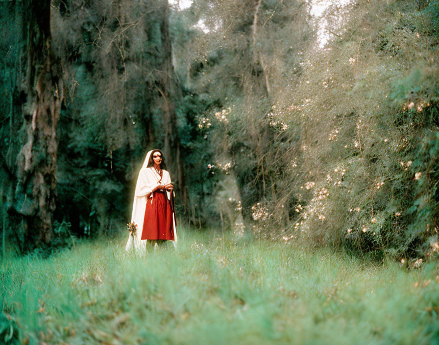 Woman in white blouse and red skirt holding wildflower bouquet in lush green forest