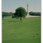 Scenic green field with people, lone tree, and historic tower on clear day