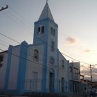 White church with blue roof and stained glass windows in serene sunset setting