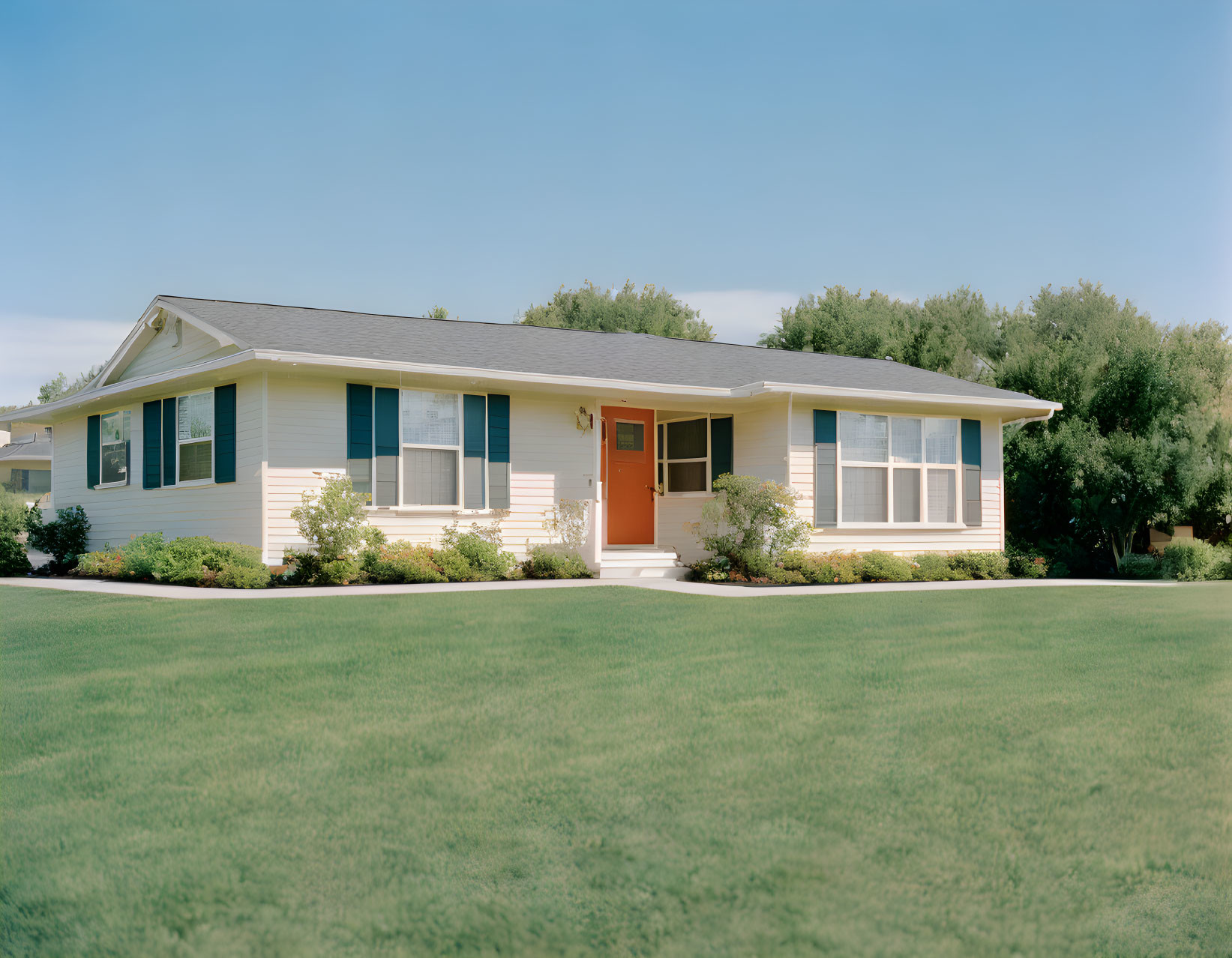 Beige suburban house with white trim, orange door, and manicured lawn