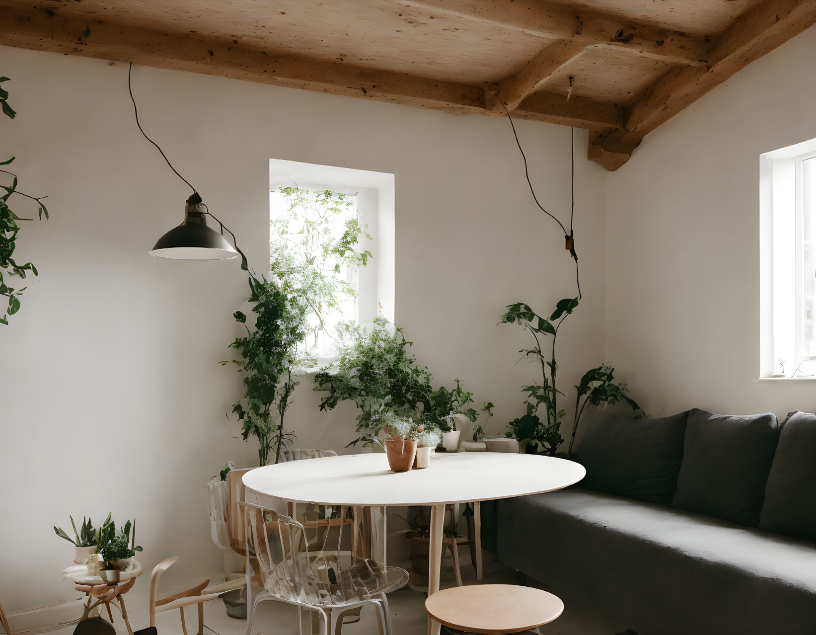 Cozy room with white walls, wooden ceiling, round table, gray sofa, green plants, pendant