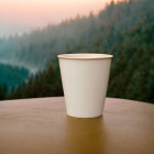 White Cup on Wooden Surface with Mountain Landscape in Soft Light