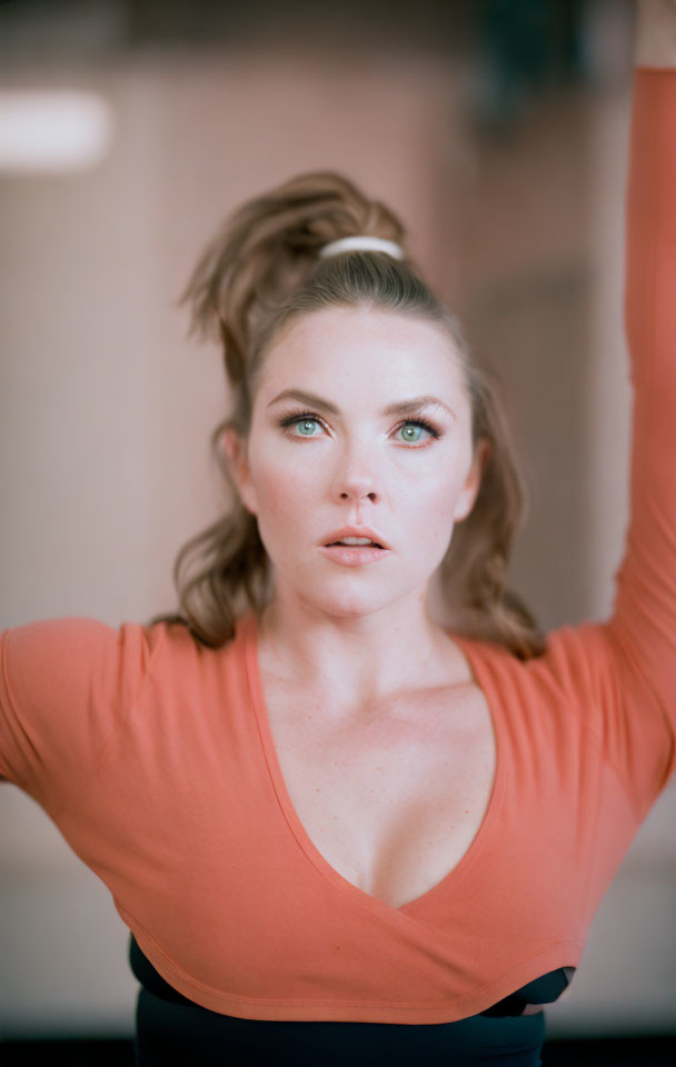 Woman in orange top with hair in bun stretching arm, gazing at camera