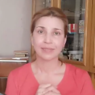 Woman in orange top with hair in bun stretching arm, gazing at camera