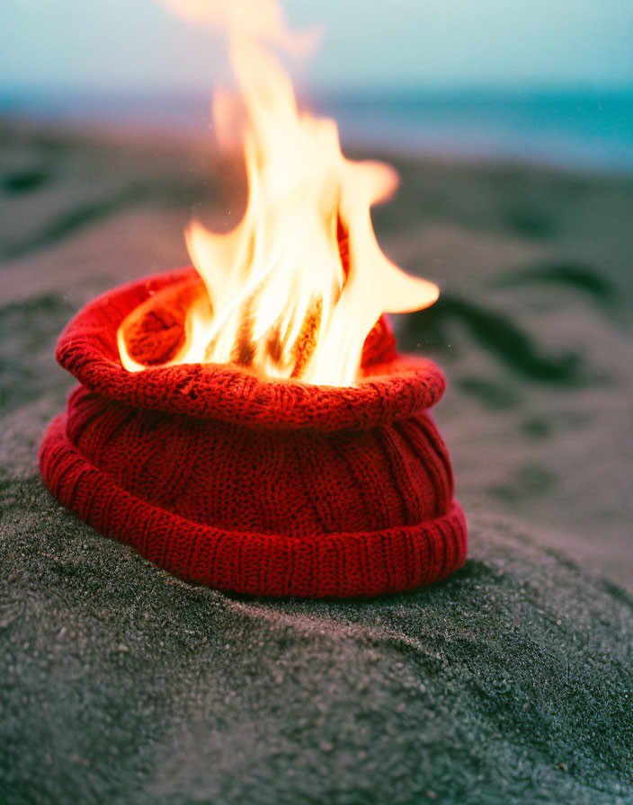 Red Knitted Beanie on Sandy Beach with Flames