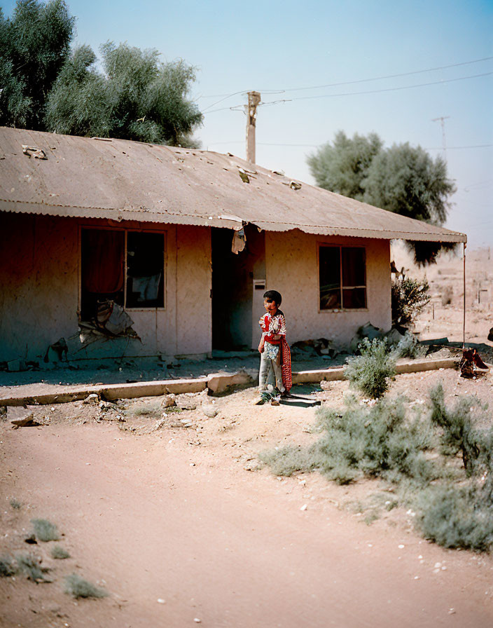 Child standing outside dilapidated building under clear sky