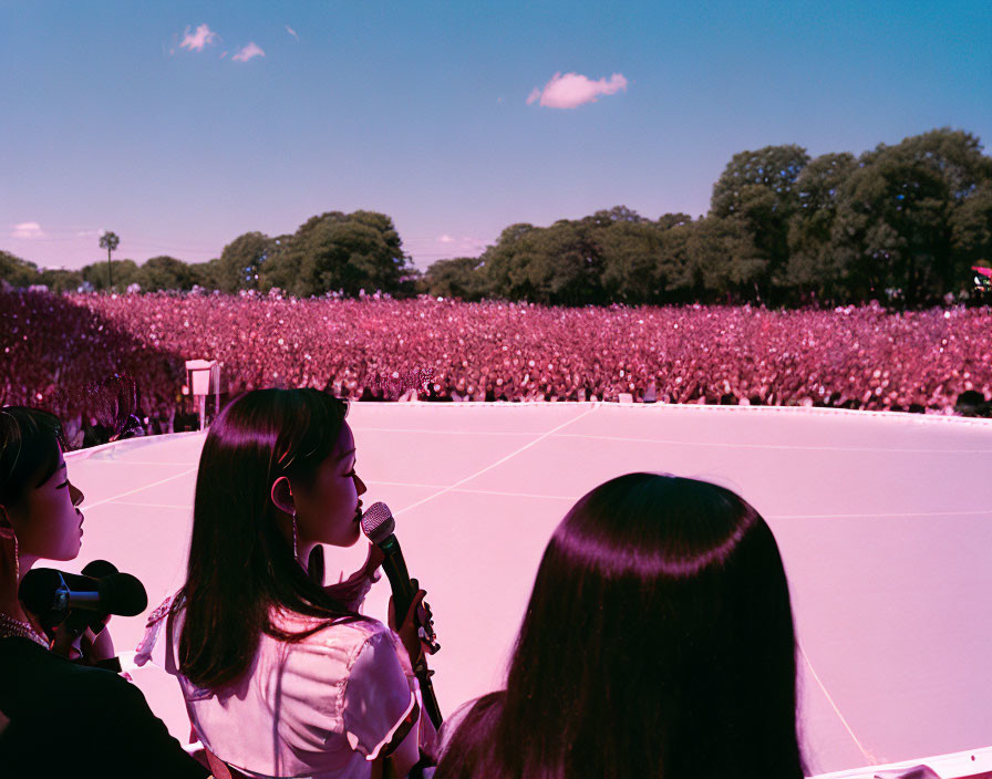 Three Individuals Holding Microphones on Stage Facing Large Audience