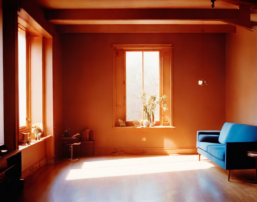 Cozy, well-lit room with orange hue, large window, blue sofa, and minimalist decor