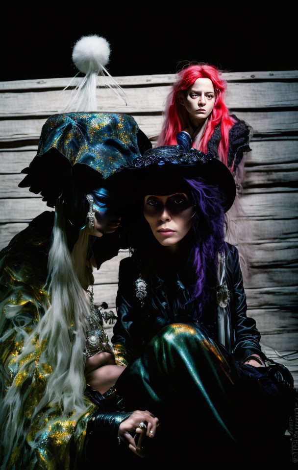 Three individuals in elaborate costumes and makeup posing in front of wooden backdrop