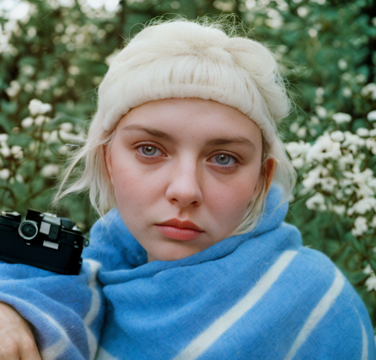 Woman with Headband Holding Camera Wrapped in Blue Striped Blanket among White Flowers