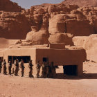 Soldiers and armored vehicles near flaming structure in desert landscape