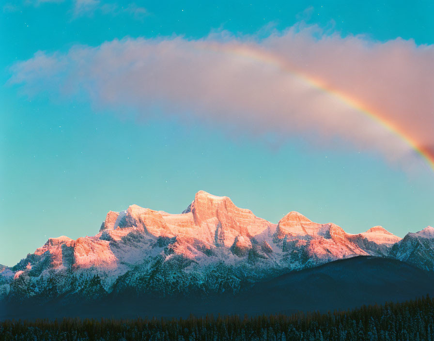 Rainbow over snow-capped mountains at sunrise or sunset