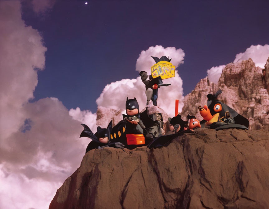 Batman figures posed heroically on rocky outcrop under dramatic sky