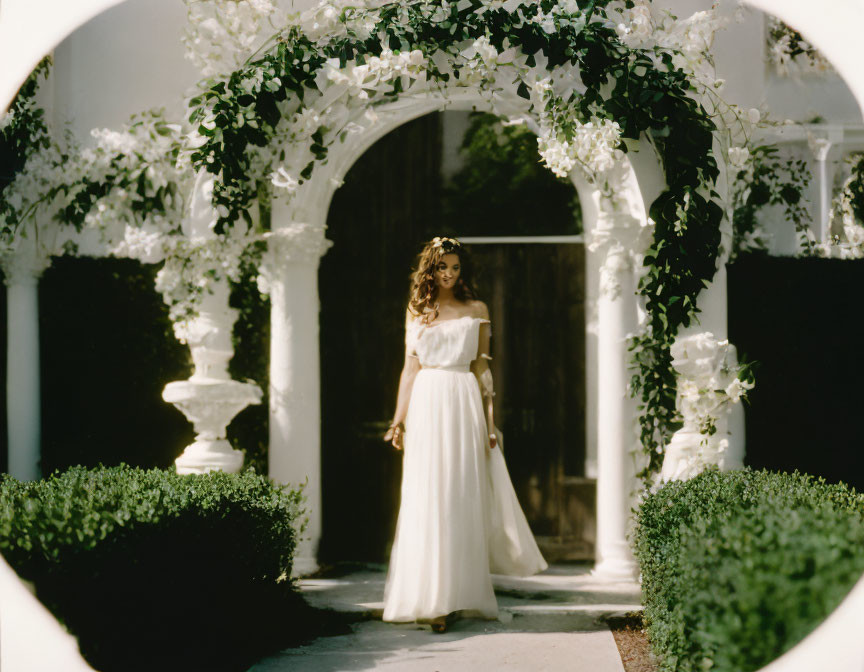 Woman in white dress under flower archway in garden