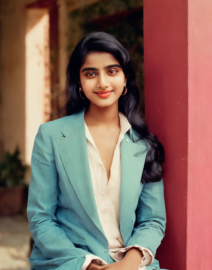 Smiling woman with long black hair in teal blazer against red pillar