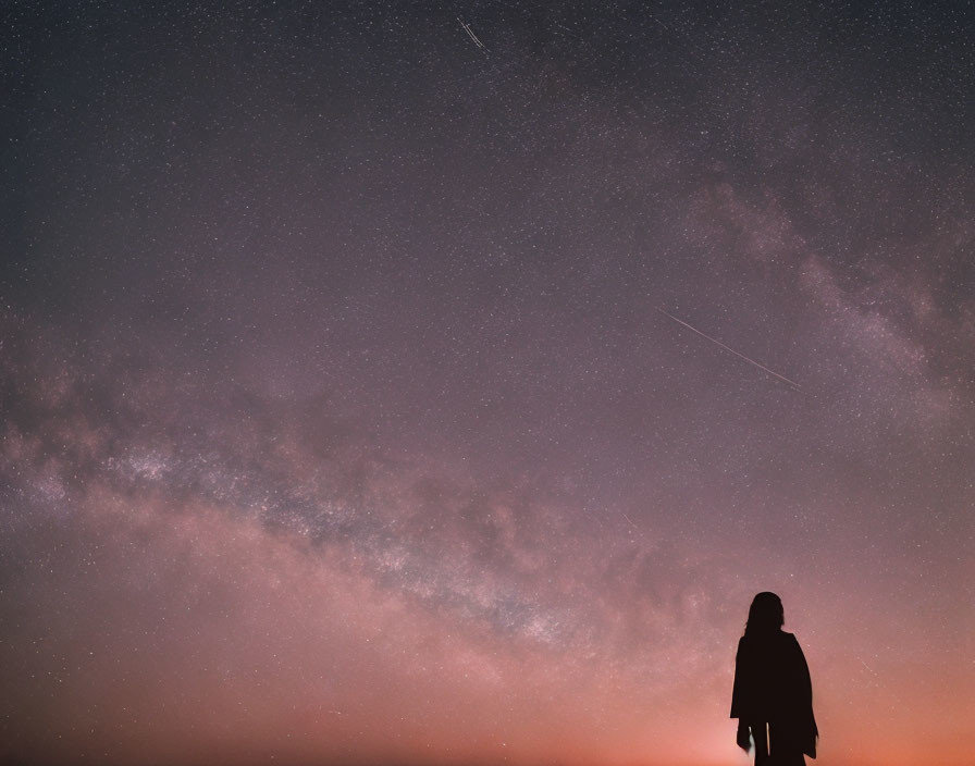 Silhouetted figure under pink and purple starry sky with shooting stars.