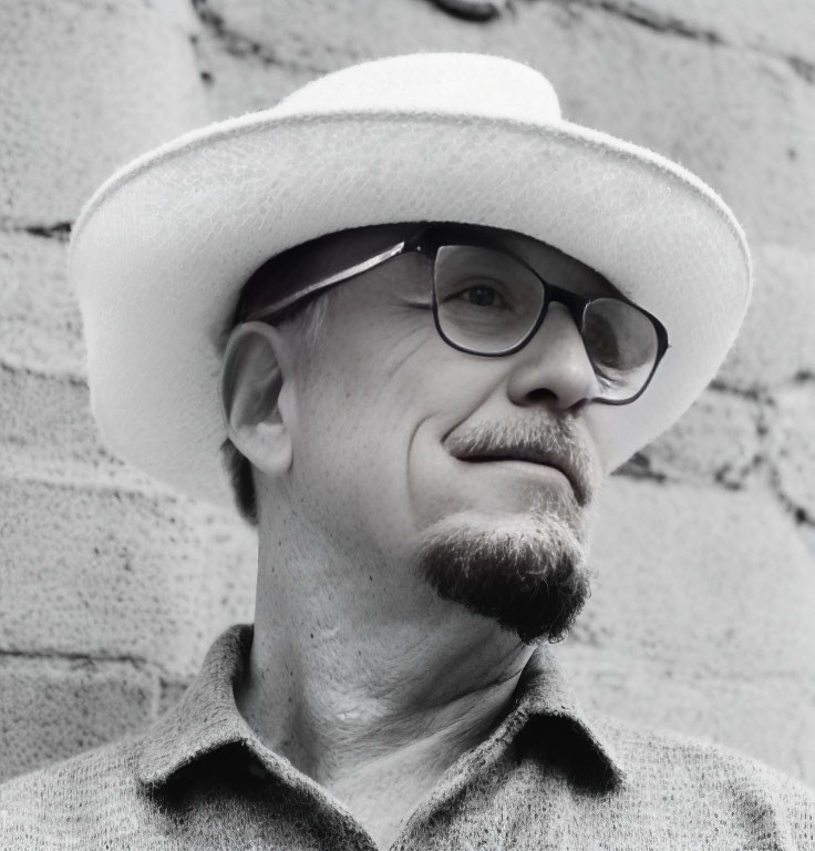 Smiling man with beard and glasses against brick wall in monochrome portrait