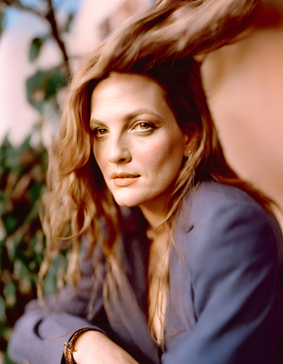 Woman with flowing hair in blue jacket against pink background with greenery