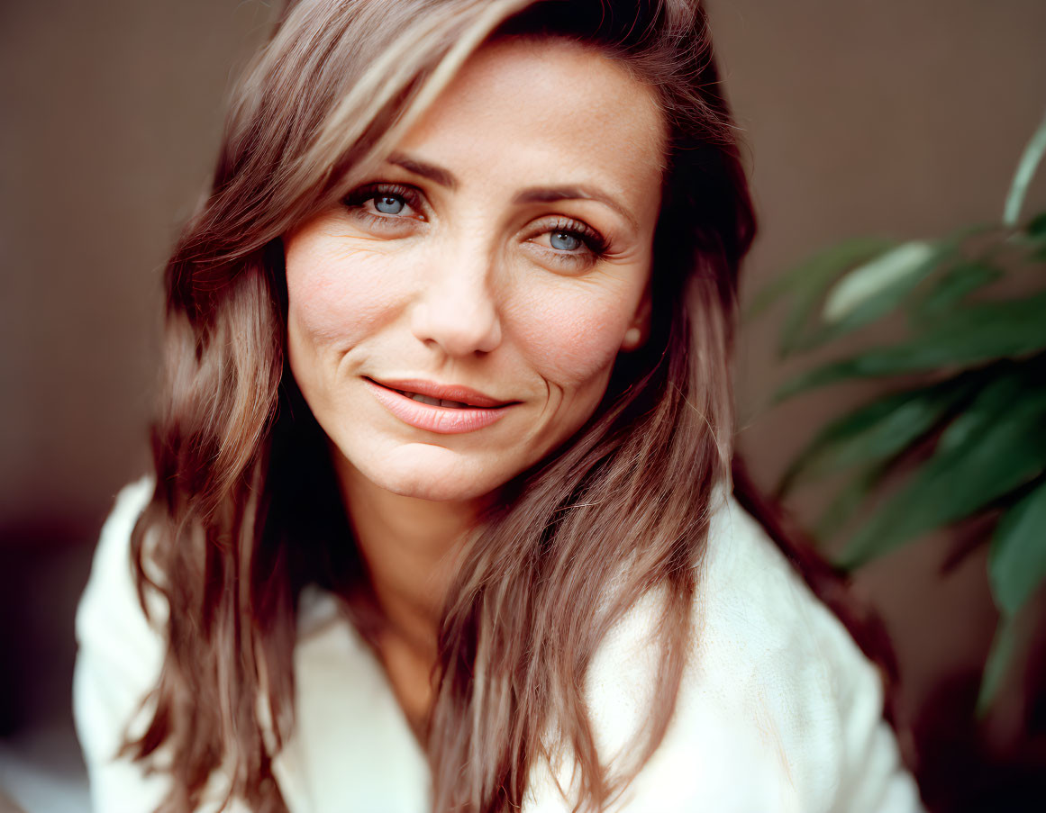 Smiling woman with long brown hair in white shirt and blurred plant background