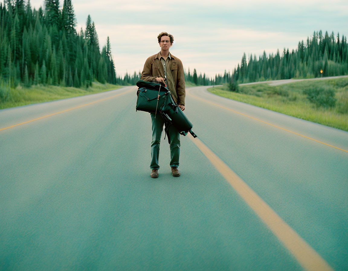 Person with bag and guitar standing on deserted road surrounded by trees