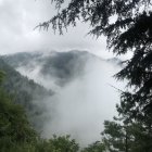 Tranquil landscape: waterfall, misty lake, lush greenery, mountains, cloudy sky