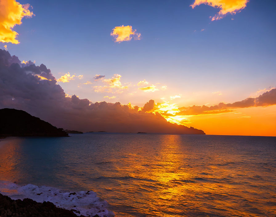 Vibrant orange sunset over ocean with silhouette of land horizon