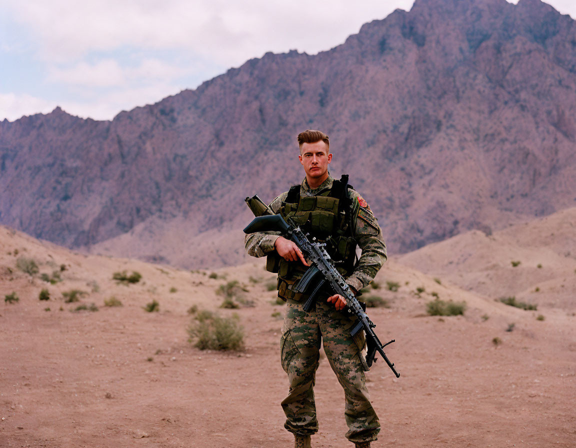 Soldier in camo gear with rifle against mountain landscape