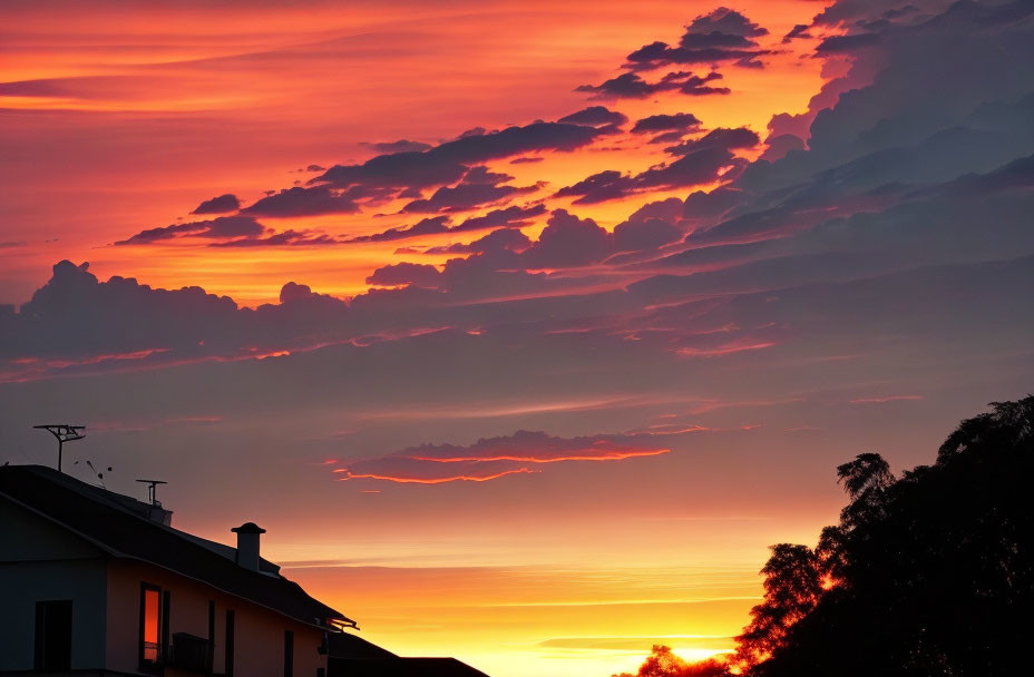 Vibrant orange and red sunset silhouettes house and clouds.