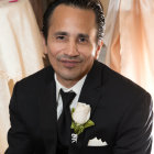 Formal man in black tuxedo with white rose boutonniere and bow tie.