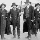 Four men in cowboy attire with hats and guns in dusty setting