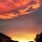 Vibrant orange and red sunset silhouettes house and clouds.