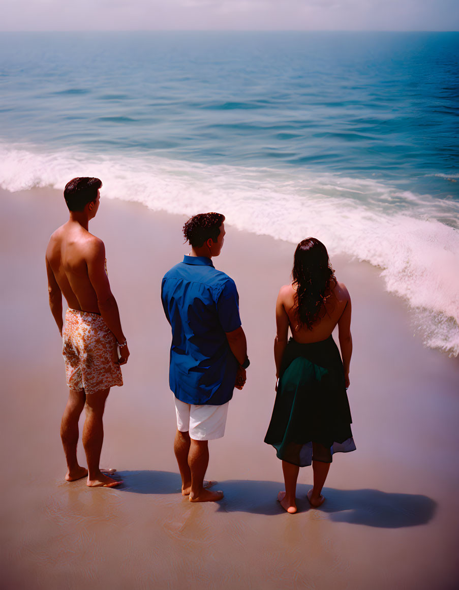 Three individuals on beach watching waves.