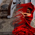 Vibrant red flamenco dress dancer in quaint alley with geranium-filled balconies