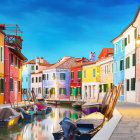 Vibrant houses along tranquil canal with boats and cobblestone path under blue sky