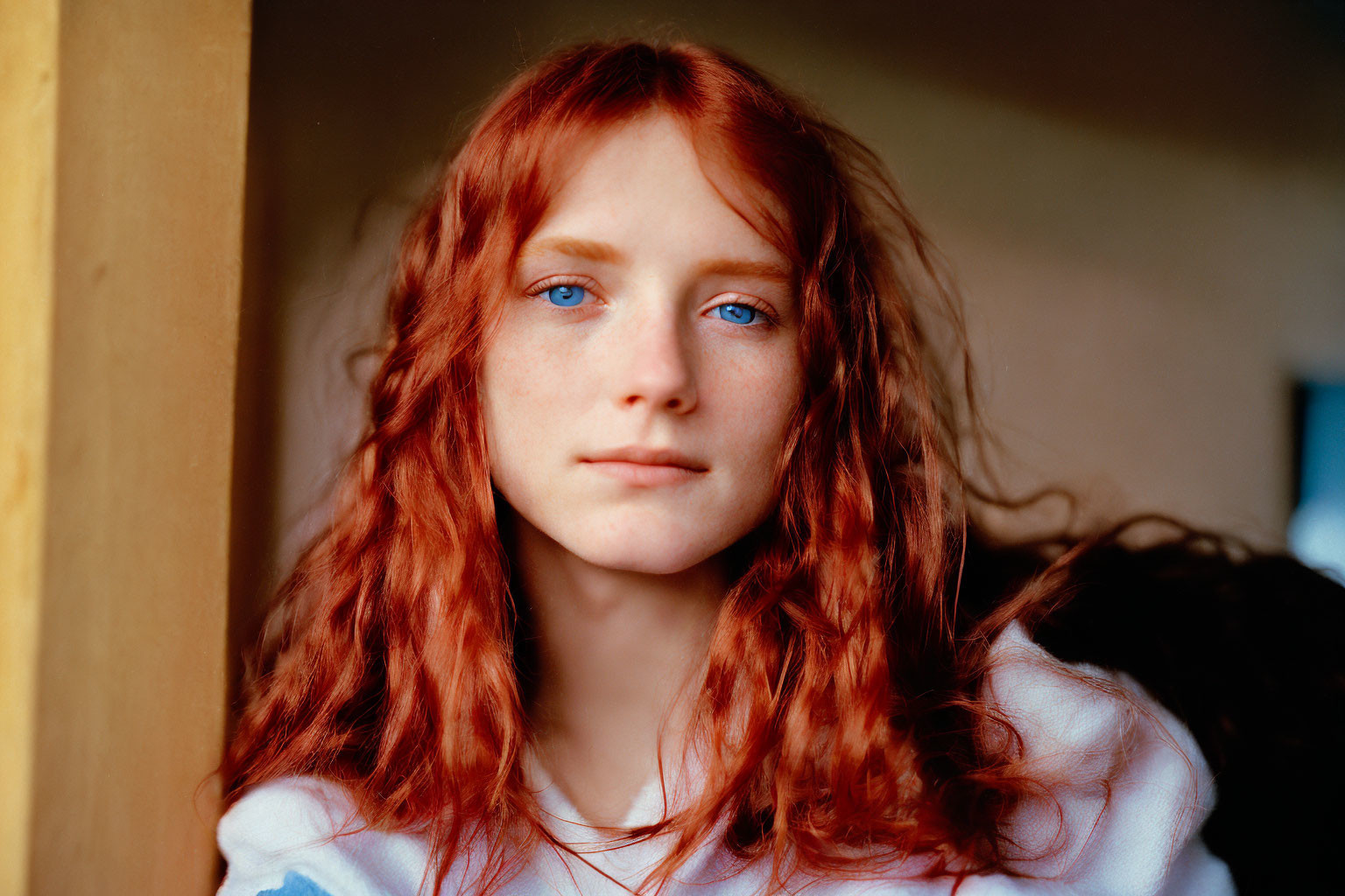 Person with Shoulder-Length Curly Red Hair and Blue Eyes in Wooden Doorway