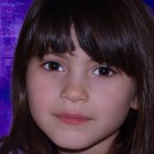 Young girl with brown hair and purple bow on rosy cheeks in purple backdrop