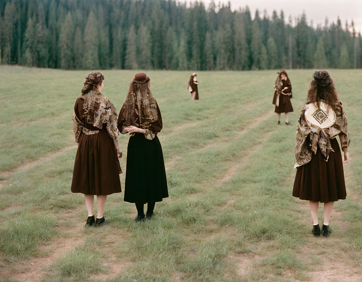 Women in traditional dresses walking in grassy clearing.