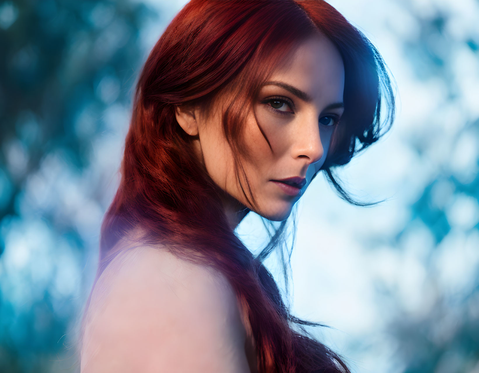 Red-haired woman with fair skin gazing, blue-tinted foliage in background