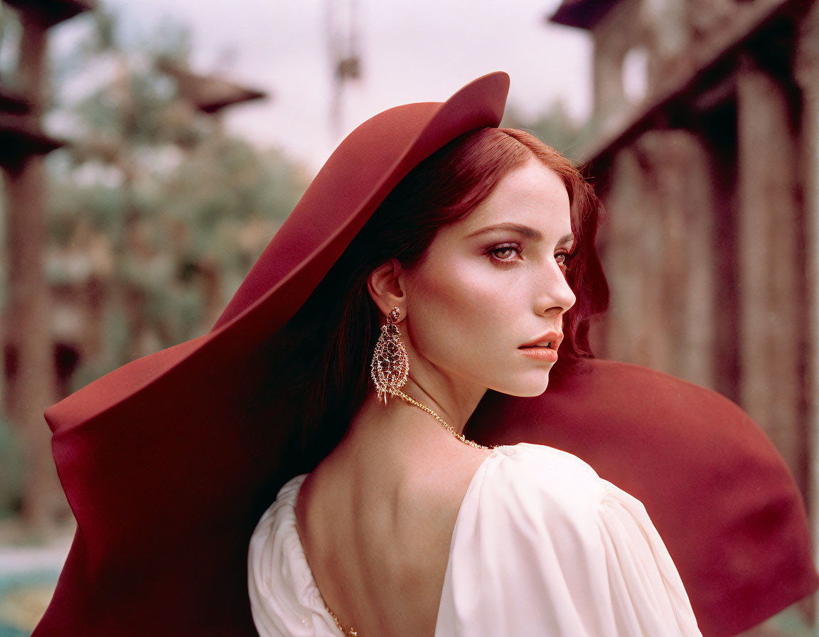 Elegant woman in red hat and off-shoulder dress against rustic backdrop