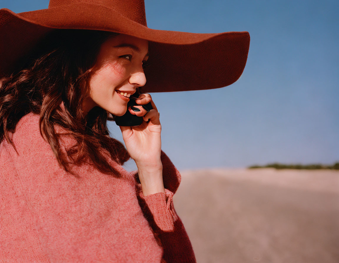 Smiling woman in wide-brimmed hat on cell phone outdoors