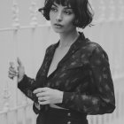 Freckled woman in floral dress with bangs holding flower in monochrome scene