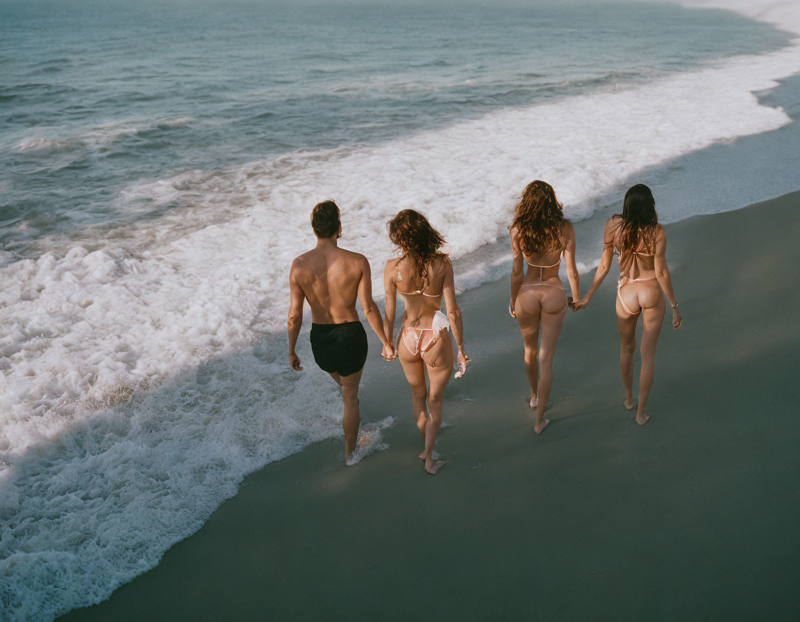 Group of four people walking on shore with waves at feet