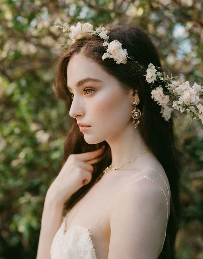 Woman with floral hairpiece and elegant earrings in greenery.