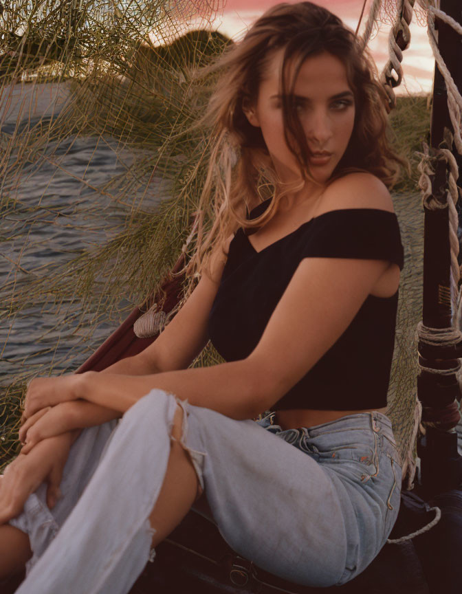 Woman in torn jeans and off-shoulder top on boat at sunset