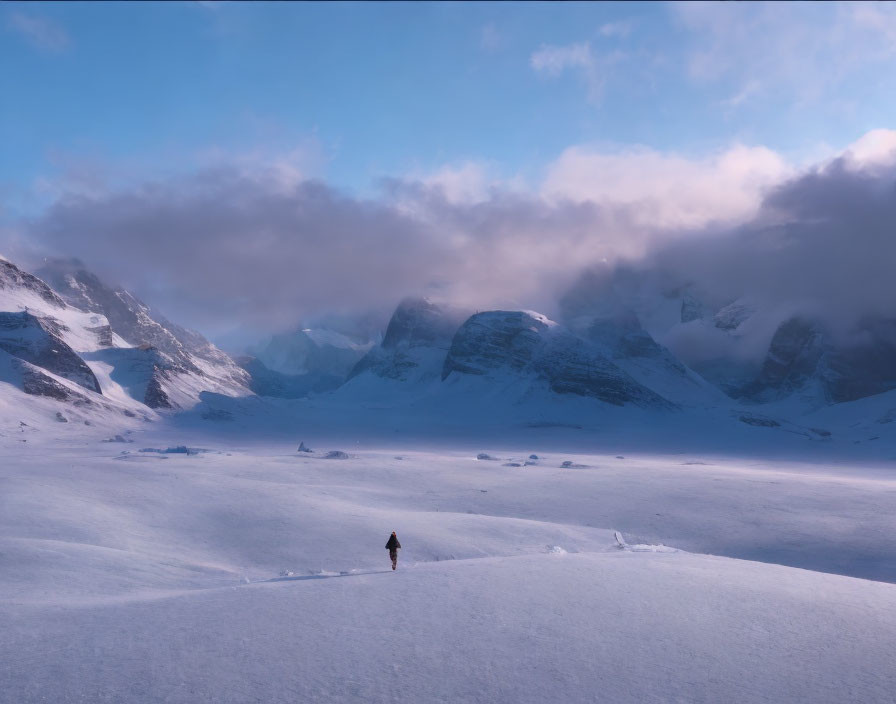 Person standing in vast snowy landscape with mountains and misty clouds.